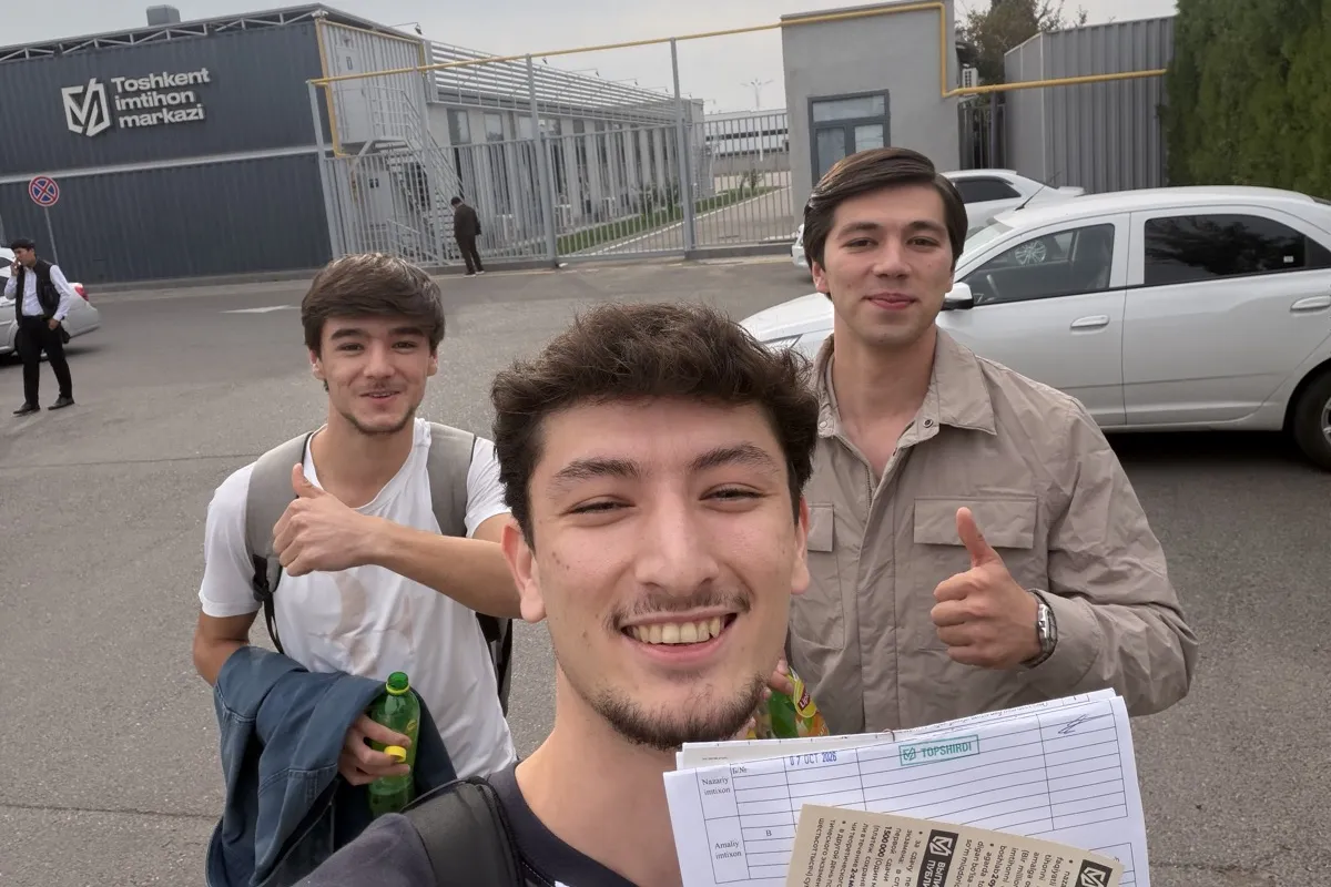 Рахмонберди Вахабов с двумя друзьями у Toshkent imtihon markazi, в руке экзаменационный лист со штампом «TOPSHIRDI», 7 октября 2026 года